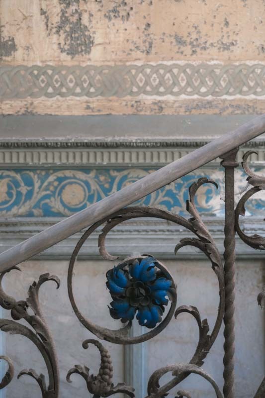 Detail of a wrought-iron railing decorated with a blue floral pattern in a decaying villa.